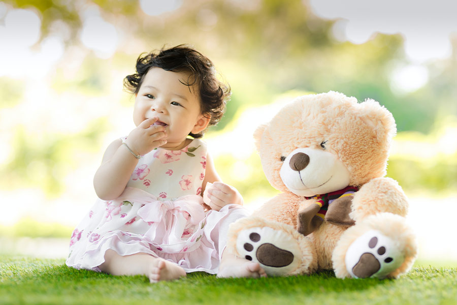 Baby sitting on grass beside bear toy