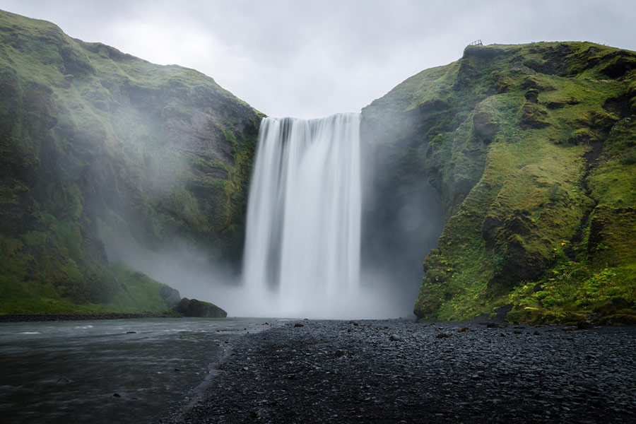 Water falls on the green covered mountain during daytime